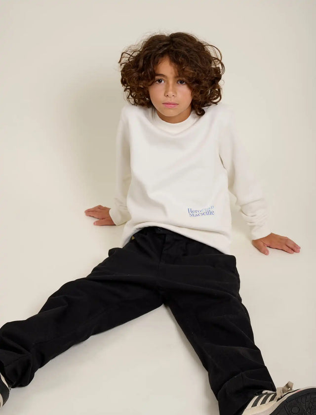 Un jeune garçon portant une chemise à manches longues crème et un pantalon noir.