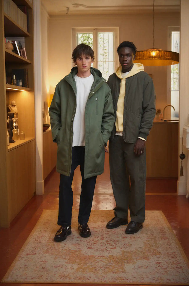 Parka vert olive avec capuche et détails de fermeture éclair noirs, fabriquée en matériau nylon.