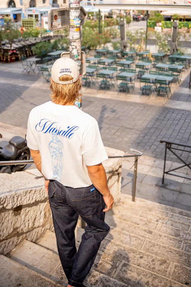 Une personne portant un t-shirt blanc avec une écriture bleue et un jean bleu foncé.